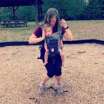 A mom sits on a swing with her son in a front carrier