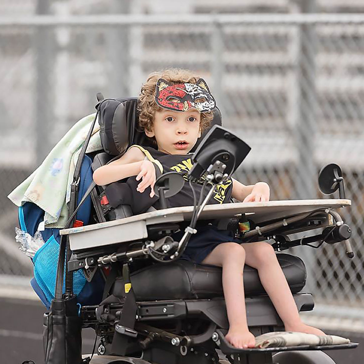 Bennett in his power wheelchair. He wears a cat mask on top of his curly brown hair.