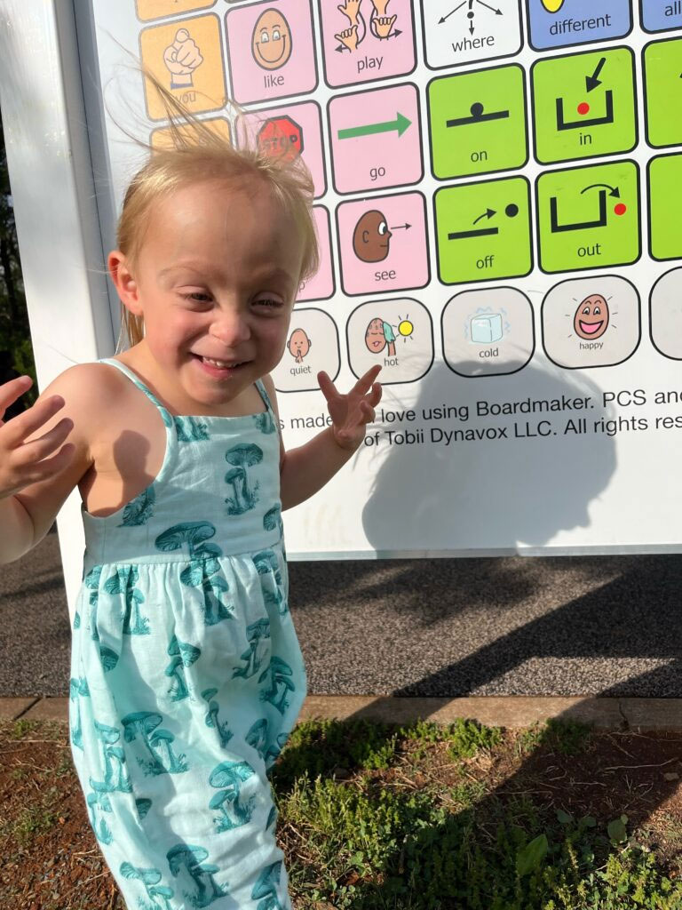 Darlene smiles in front of the Communication Board at Pen Park.